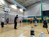 Two singles matches of badminton being played on half a court each