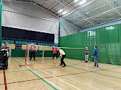 Two matches of badminton being played on half a court each